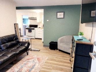 Anchorage apartment for rent - A black leather sofa sits in a living room with a rug and a kitchen in the background.