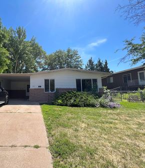 Fort Collins apartment for rent - A house with a white exterior and a brown roof is surrounded by greenery and a clear blue sky.