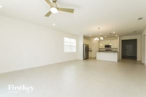 Kissimmee house for rent - A spacious, empty room with a ceiling fan and a kitchen area in the background.