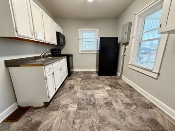 New Albany apartment for rent - A kitchen with a black fridge, white cabinets, and a window.
