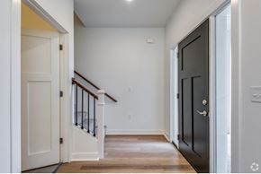 Oshkosh townhouse for rent - an empty room with a black door and a hallway with wood floors and a staircase