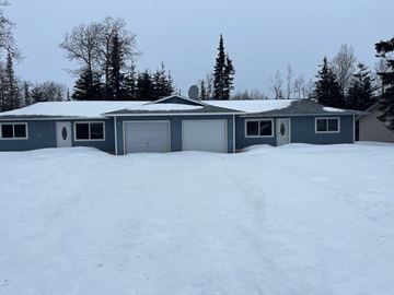Kenai apartment for rent - A house with a grey roof and a garage door is surrounded by snow.