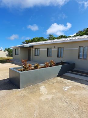 Yigo apartment for rent - a white house with a concrete wall and plants in front of it
