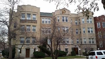 Chicago apartment for rent - A large, beige building with a green roof and a white car parked in front.