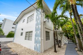 Miami apartment for rent - A white house with blue patterns on the side is surrounded by palm trees.