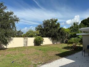 Bradenton house for rent - a backyard with a yellow wall and a lawn and trees