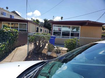 National City apartment for rent - A white car is parked in front of a house with a blue sign on the fence.