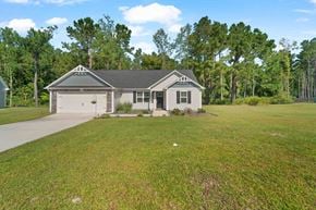 Jacksonville house for rent - A house with a grey roof and a garage is surrounded by a grassy area and trees.