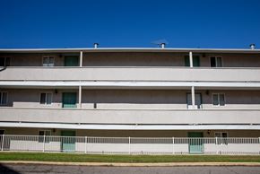 Orem apartment for rent - the side of a white building with green doors and a white fence