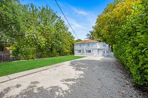 Miami apartment for rent - A gravel driveway leads to a white house surrounded by greenery.