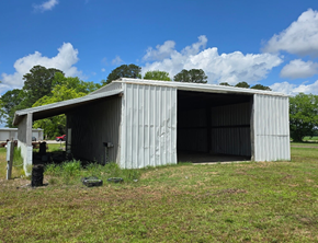 Chadbourn apartment for rent - A large, grey metal shed sits in a grassy field under a blue sky with clouds.