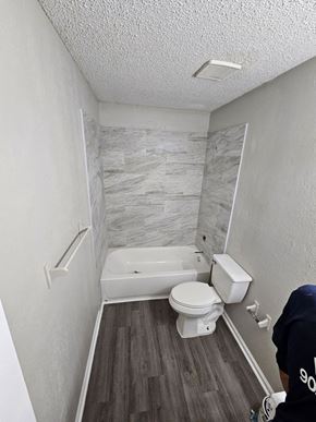 Hughes Springs house for rent - A man in a black shirt with the number 900 is standing in a bathroom with a white toilet and a bathtub.