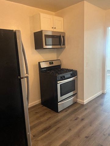 Los Angeles apartment for rent - A black refrigerator is in the corner of a kitchen with a black stove and microwave above it.