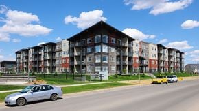 Saskatoon apartment for rent - A silver car is parked on the side of a road in front of a large apartment building.