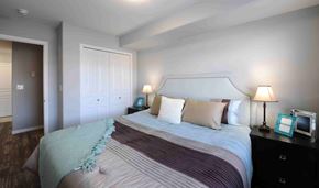 Saskatoon apartment for rent - A bedroom with a large bed and a nightstand with a lamp.