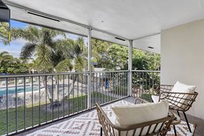 Boca Raton apartment for rent - A balcony with a chair and a cushion overlooking a pool and trees.
