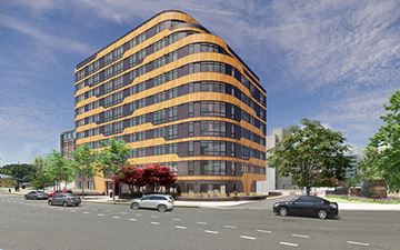 Washington apartment for rent - A modern building with orange and black windows is surrounded by trees and cars on the street.