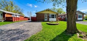 Trenton apartment for rent - A small house with a yellow roof is surrounded by a gravel driveway and a grassy area with a tree.