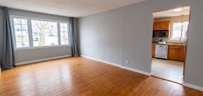 Trenton apartment for rent - A large empty room with wooden floors and a view of a kitchen through an open door.
