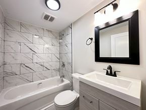 Trenton apartment for rent - A white bathroom with a marble tile wall and a white tub and toilet.