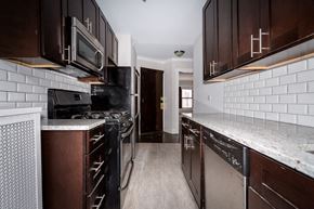 Chicago apartment for rent - a kitchen with black appliances and white tiles and wooden cabinets