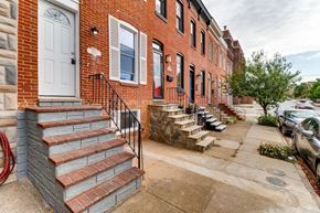 Baltimore house for rent - A red brick house with a white door and a black iron railing.