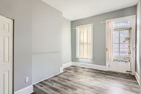Baltimore apartment for rent - A room with a wooden floor and a window with white curtains.