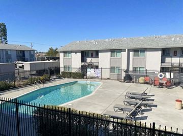 Victorville apartment for rent - A pool surrounded by a black fence and chairs.