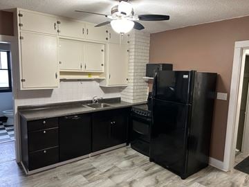Prince Albert house for rent - a kitchen with black appliances and white cabinets and a ceiling fan