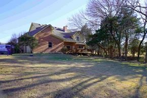 Rockwall house for rent - A house with a red brick exterior and a grey roof is surrounded by trees and grass.