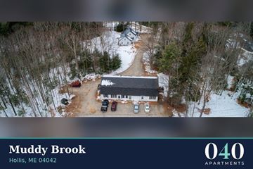 Hollis apartment for rent - An aerial view of a parking lot with cars and a building with the text "Muddy Brook Hollis, ME 04042" and "040 Apartments" on it.