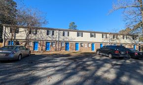 Little Rock apartment for rent - an old brick building with blue doors and cars parked in front