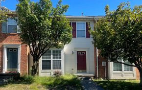 Winchester townhouse for rent - A white house with a red door is surrounded by green trees.