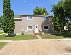 Wahpeton apartment for rent - A house with a brown siding and a white door is surrounded by trees.