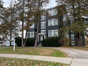 Poughkeepsie apartment for rent - A black building with white windows and a white door is surrounded by trees.