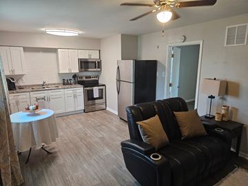 Killeen apartment for rent - A black leather couch with two pillows sits in a living room with a kitchen in the background.