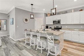 Estero house for rent - a kitchen with white cabinets and a bar with three chairs