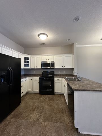 Clarksville house for rent - an empty kitchen with white cabinets and black appliances