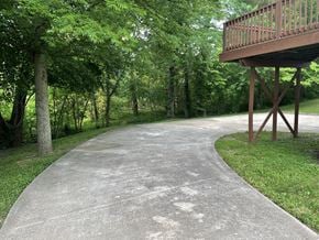 Clarksville house for rent - A concrete walkway leads to a wooden deck surrounded by trees.