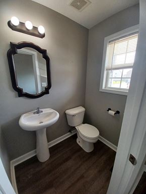 Clarksville house for rent - A bathroom with a toilet, sink, mirror, and light fixture.