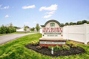Indiana apartment for rent - the sign for hickory meadows in front of a white fence and grass
