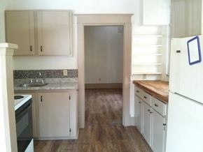 Victoria apartment for rent - an empty kitchen with white cabinets and a door to the living room