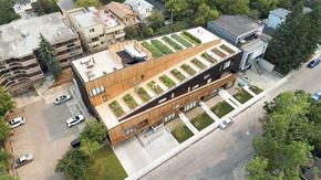 Calgary apartment for rent - A modern building with a green roof is surrounded by other buildings and trees.