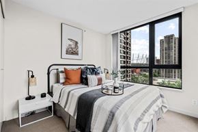 Vancouver apartment for rent - A bedroom with a large bed and a view of a city skyline through the window.