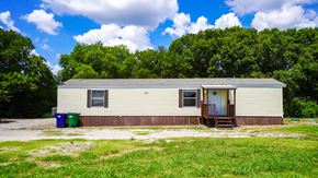 Royse City apartment for rent - A small house with a brown roof and a white door is surrounded by greenery.
