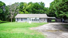 Royse City apartment for rent - A house with a grey roof and white walls is surrounded by green grass and trees.
