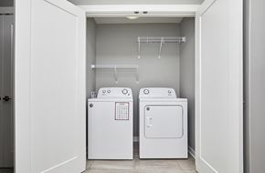 Waukee apartment for rent - A white laundry room with two washing machines and a shelving unit.