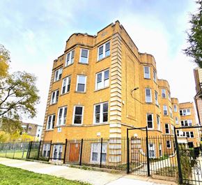 Chicago apartment for rent - A large brick building with a black fence in front.