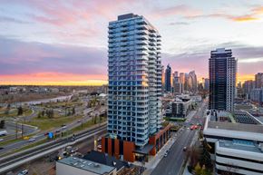 Calgary apartment for rent - A tall, modern building stands in the foreground of a cityscape at sunset.