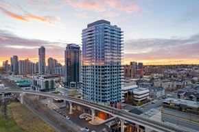 Calgary apartment for rent - A modern high-rise building is the focal point of a bustling cityscape at dusk.